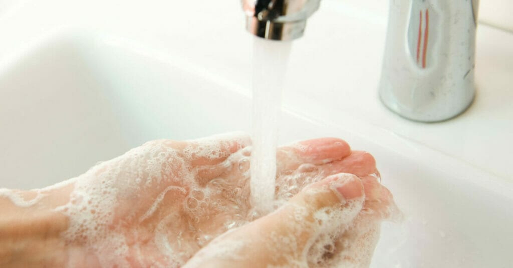 A person removing dirt and bacteria from their hands with soap in a sink.