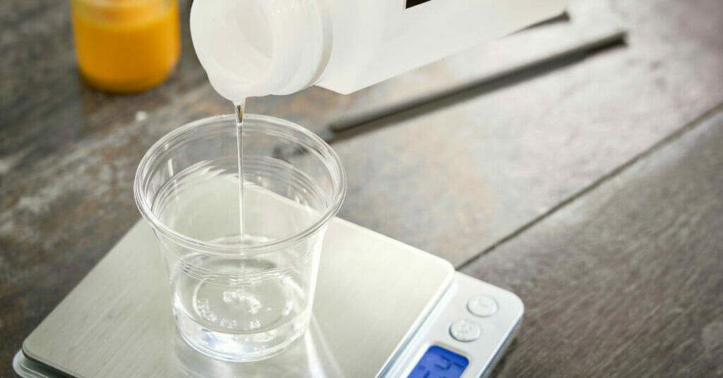 A person meticulously pouring epoxy resin into a glass on a scale, ensuring the perfect measurement for their project.