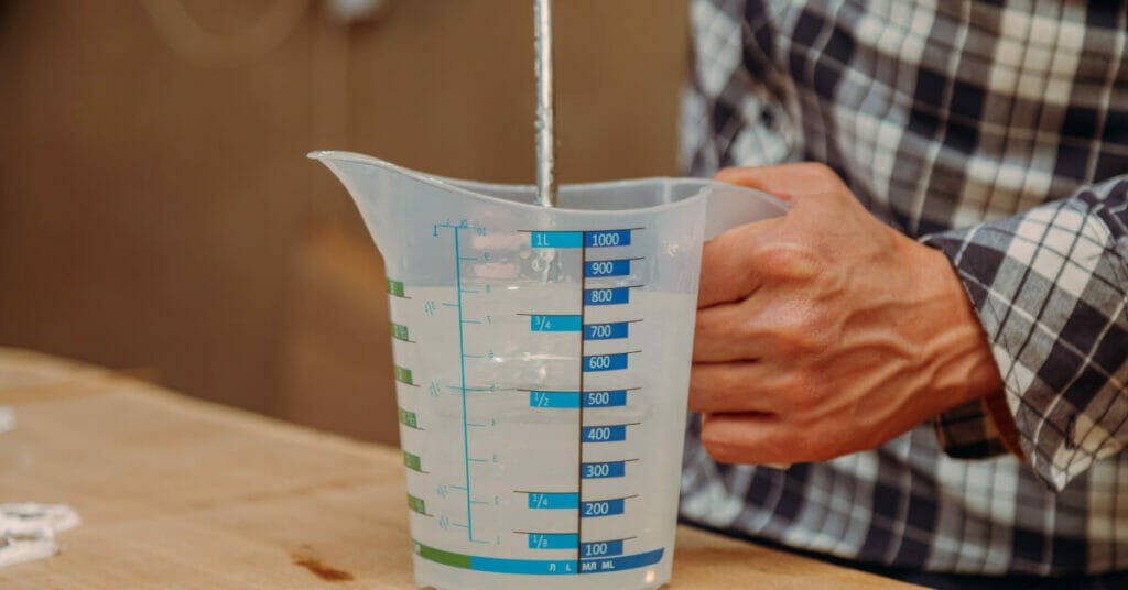 A man pouring epoxy resin into a measuring cup.