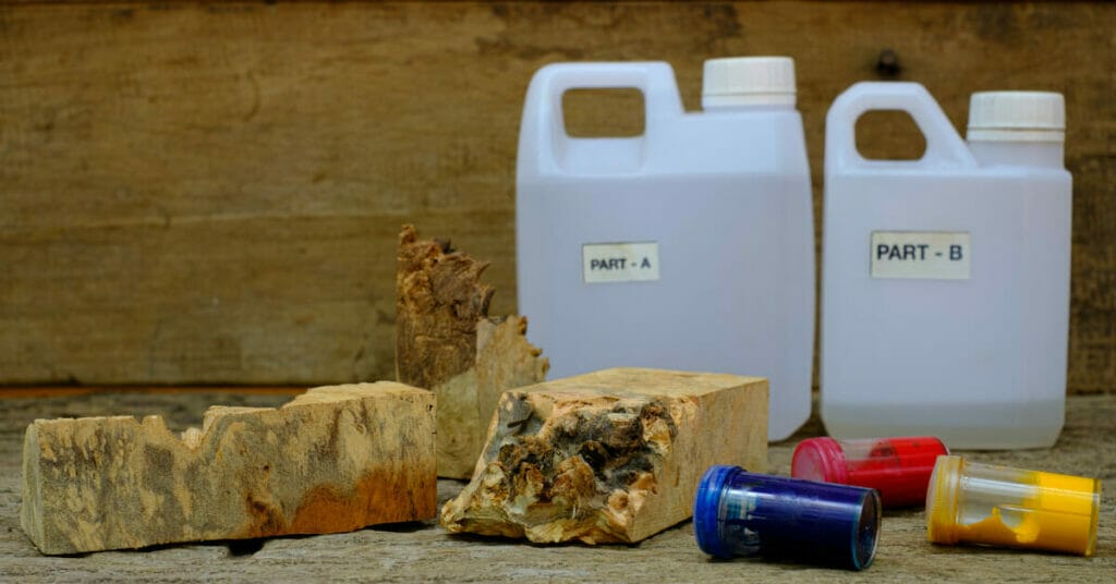 A bottle of epoxy resin, a bottle of water, and a piece of wood.